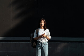 University student in white shirt holding smartphone.