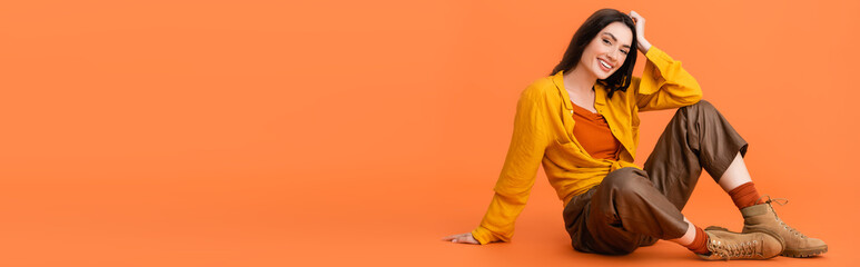 panoramic concept of brunette and trendy woman in autumn outfit sitting on orange