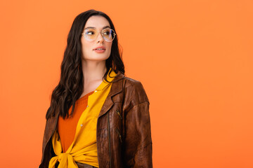 young woman in autumn outfit and glasses looking away isolated on orange
