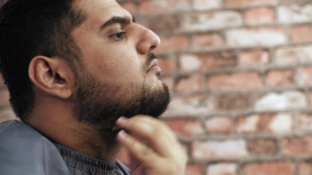 Caucasian man combing beard with comb on brick wall background. Close up face bearded man combing black beard