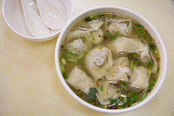 Top view of a traditional Chinese dumplings soup, with scallion, in a white bowl 