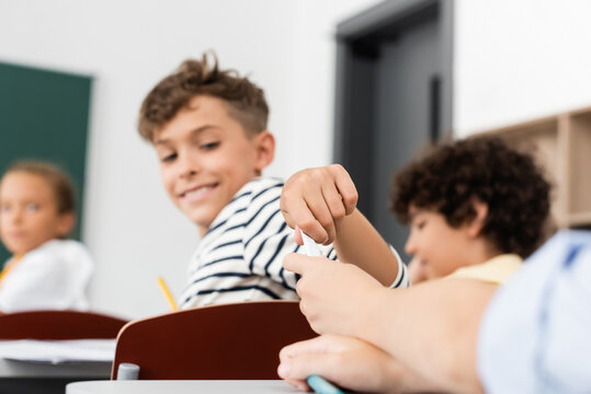 cropped view of schoolkid passing note to classmate near multicultural pupils during lesson