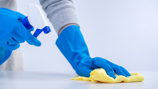 Young Woman Housekeeper In Apron Is Cleaning, Wiping Down Table Surface With Blue Gloves, Wet Yellow Rag, Spraying Bottle Cleaner, Closeup Design Concept.