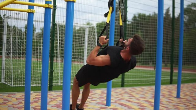 Caucasian sportsman doing pull ups exercise using rubber belt to force strenth of workout outdoors