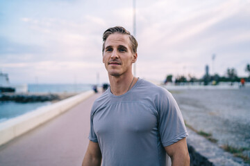 Serious caucasian male runner in activewear having cardio training on coastline in morning enjoying healthy lifestyle, determined energetic man jogger keeping fit and physical strength on workout