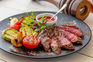 chopped medium rare steak with grilled vegetables. Sauce is served with the dish. Dish on a white plate in natural light.