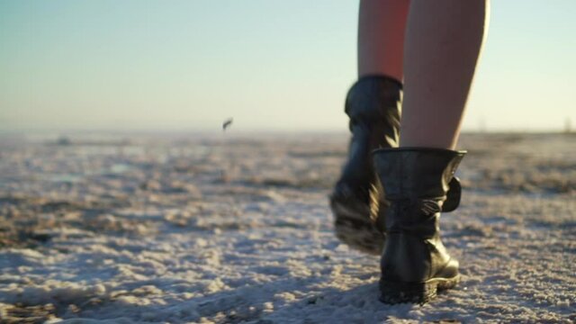Close-up of female legs in boots are walking on the ground. Rear view, tracking camera. Slow motion.