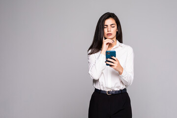Pretty business woman in formal wear smiling and holding cell phone isolated over gray background