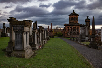 Scotland. Glasgow Necropolis Hill in nasty day. Grave monuments and mausoleum. Green grass and yellow trees. Grey storm cloudy sky. Panorama view.