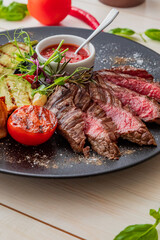 chopped medium rare steak with grilled vegetables. Sauce is served with the dish. Dish on a white plate in natural light.