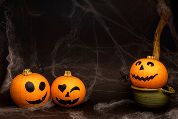 Little orange pumpkins with painted faces for Halloween with spiders on the net on black background