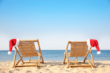 Sun loungers with Santa's hats on beach, space for text. Christmas vacation