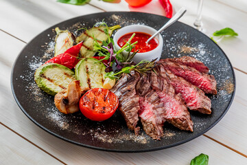 chopped medium rare steak with grilled vegetables. The dish is served with tomato sauce and a glass of red wine. Dish on a white plate in natural light.