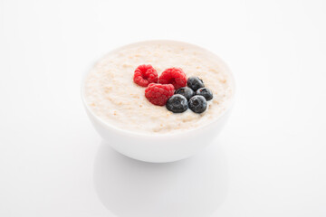 Oatmeal porridge with raspberries and blueberries on a white background