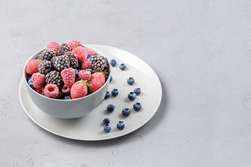 Frozen berries in a grey bowl on a grey concrete background.