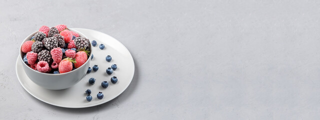 Frozen berries in a grey bowl on a grey concrete background with copies of space.