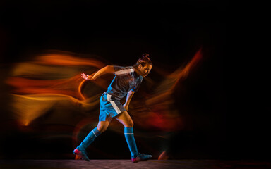 In fire. Football or soccer player on black studio background in mixed light. Young male sportive model training in action. Kicking ball, attacking, catching. Concept of sport, competition, winning.
