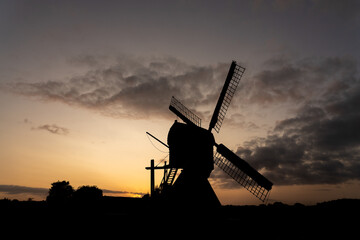 Silhouette of a traditional Dutch windmill against the red orange light of the rising or setting sun