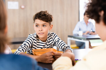 selective focus of schoolboy sitting in school eatery near classmates