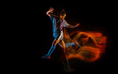 Jump high. Football or soccer player on black studio background in mixed light. Young male sportive model training in action. Kicking ball, attacking, catching. Concept of sport, competition, winning.