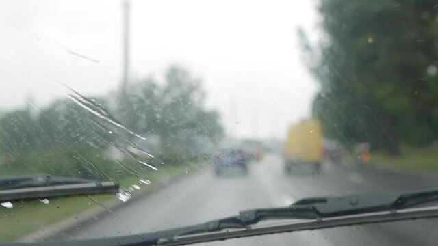 Wipers clean the windshield of the car on the go during heavy rain. Inside blurred view of a country road. Driving in difficult weather conditions