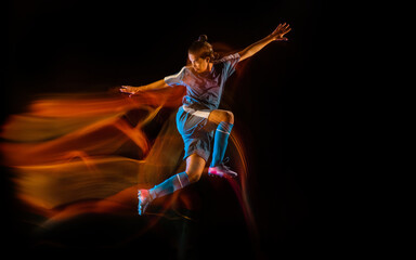 Flying high. Football or soccer player on black studio background in mixed light. Young male sportive model training in action. Kicking ball, attacking, catching. Concept of sport, competition