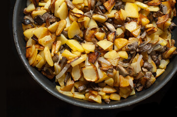 Fried young potatoes with mushrooms and onions. View from above. In a skillet. On a black background.