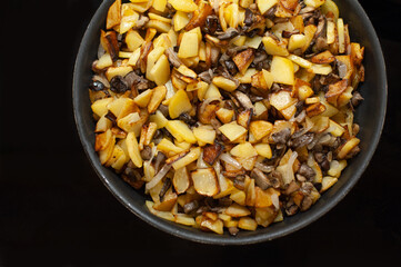 Fried young potatoes with mushrooms and onions. View from above. In a skillet. On a black background.