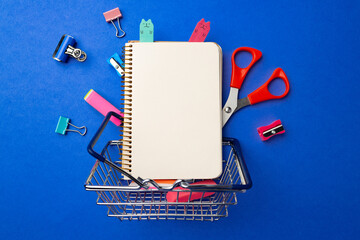 School supplies in a shopping cart on blue background