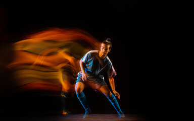 Fototapeta na wymiar Winning. Football or soccer player on black studio background in mixed light. Young male sportive model training in action. Kicking ball, attacking, catching. Concept of sport, competition, winning.