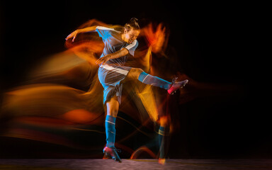 Winning. Football or soccer player on black studio background in mixed light. Young male sportive model training in action. Kicking ball, attacking, catching. Concept of sport, competition, winning.