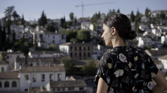 Mujer joven morena en un mirador observando la vista panorámica de la ciudad de Granada en un día soleado HD