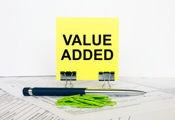 Yellow sticker with text Value Added stands on office clips. Next to it is a blue pen with green...