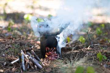 Obraz premium fire and smoke in the camp wood stove from the tin can, coffee in the can, firewoods near a stove