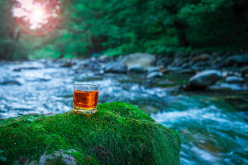 Whiskey in a glass on the stone with moss in river background