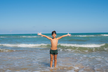 Fototapeta na wymiar Happy child boy raised hands on sea beach