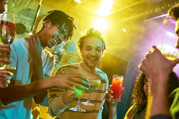 Feel the party. Cropped shot of a group of friends, young women and men toasting while having fun,...