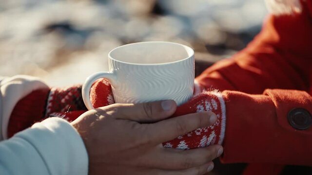 Close up hands of couple holding cups with hot tea at winter days. Coffee in the hands of a girl and a guy at xmas date. Freezing weather and warm hugs. Love concept.