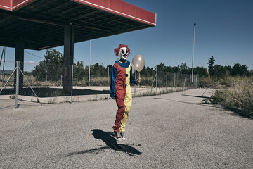 scary clown with a golden balloon jumping outdoors