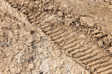 Tyre track and human footprint on sand texture background. Traces of off-road tires. Cracked earth on country road with traces of tires, cars, cracks and dirt. To use as background