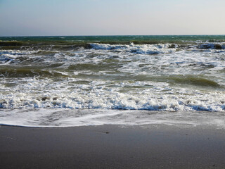 Huge stormy waves crashing near city embankment, dramatic sky on background. Big sea wave splash. Giant waves on stormy