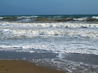 Sand on the beach and sea foam. White foam on sandy beach. Closeup of beach and sand texture from  Soft wave of blue ocean on sandy beach. Background. Copy space