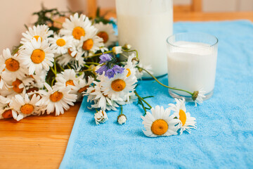 Simply stylish wooden kitchen with bottle of milk and glass on table, summer flowers camomile, healthy foog moring concept