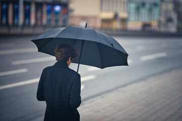 Young man hanging black umbrella, rainy weather. Stylish man with umbrella in rainy foggy day walking alone down the city street. Person with umbrella stands by road in rainy weather.