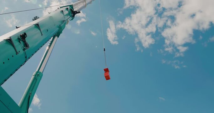 An orange building cradle lifted by a mobile crane lifts up. Slow motion.