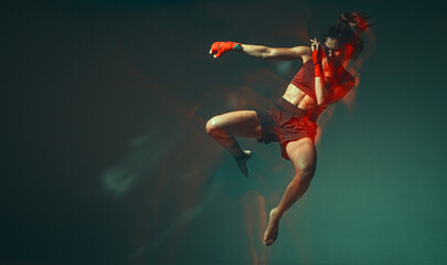 Fototapeta na wymiar Cool female fighter jumping levitating in neon light in stylish sportswear. Women's sport concept. Long exposure shot