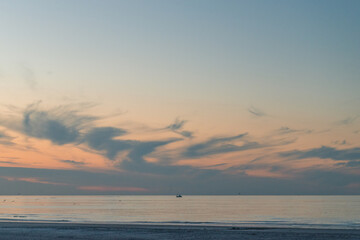 Fishing boat on the horizon on a ry sunset with some clouds on the beach of Ameland in the Netherland, idillic beautiful colors nature photo