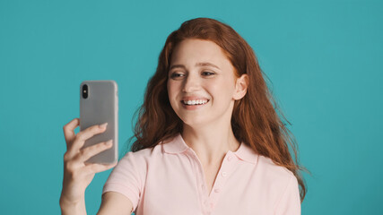 Fototapeta premium Pretty cheerful girl happily talking on video call with friends on smartphone over colorful background