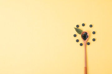 spirulina in tablets with wood spoon and jar on yellow background. Concept natural, eco, powder healthy dietary supplement. Copyspace.