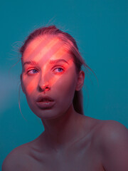 Trendy portrait of young pretty girl with coral light pattern from blinds on her face isolated on blue studio background